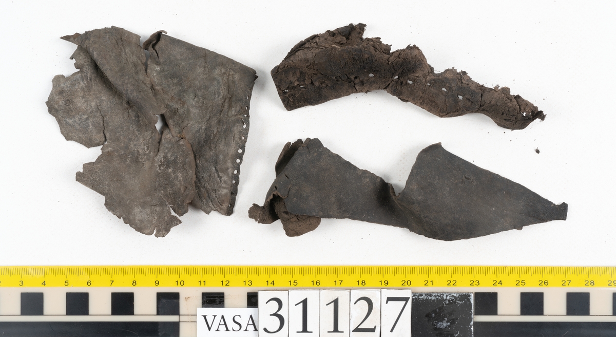 Delar och fragment från sko: tre sulor, en holtrand, en klacklapp, en klacklapp eller ett inlägg samt ett 40-tal delar och mindre fragment från skoöverdel och skobotten.

Sula fyndnummer 31127 har kvarsittande tråd. På sulans ovansida finns intryck av bindtråden.  Sula fyndnummer 31127:1 har kvarsittande träpligg och tråd. I tåpartiet finns en laglapp. Sulans hälparti är avskuret, eventuellt avbrutet.  Sula fyndnummer 31127:2 har ett fragmentariskt hälparti. På sulans ovansida finns intryck av bindtråd. Holtrand fyndnummer 31127:3 har kvarsittande tråd. På klacklapp fyndnummer 31127:4 finns hål efter träpligg. På klacklapp, eventuellt inlägg, fyndnummer 31127:5 finns kvarsittande tråd.