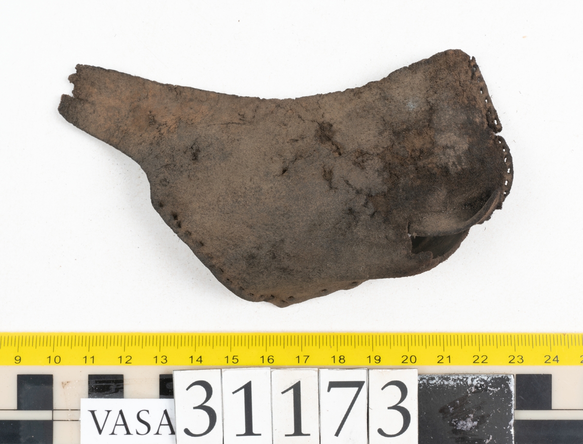 Dokumentation 1998:
Fem delar av överdelen till en slejfsko.
Ett ovanläder med bred och kantigt skuren plös, fyndnummer 31173. Längs med ovanlädrets ena sida och tvärs över tåpartiet löper stygnshål. Längs med ytterkanterna löper hål efter träpligg och stygn. Ovanlädrets främre parti och plös är något fragmentarsika. Lädret är kraftigt med fläckvisa, rostfärgade utfällningar.
En skuren läderremsa, fyndnummer 31173. Remsan har suttit fästad längs ovanlädrets ena sida. Längs med remsans ytterkanter löper hål efter stygn och träpligg.
Två stycken sidostycken med slejf. Sidostyckena har slutit om hälpartiet och fästats samman med en söm mitt bak på skon. Det vänsta sidostycket, fyndnummer 31173:1, är det bäst bevarade. I slejfänden finns ett urtag, troligtvis ett knapphål. Längs med ytterkanterna löper hål efter stygn. Längs den nedre kanten löper hål efter träpligg. Det högra sidostyckets nedre del samt slejfände är fragmentarisk. Lädret är kraftigt och relativt välbevarat.
En förstärkning, fyndnummer 31173:2. Troligtvis har lädret suttit fästat på ovanlädret och förstärkt tåpartiet. Lädret är kraftigt.

Dokumentation 2022:
Del av ovanläder. Framstycke till en sluten sko. Skapades på en rak läst och bars på vänster fot. Inga dekorationer. Fyndnummer 31173:1 är skons bakkappa och den har skador som liknar de från fyndnummer 09806. Fyndnummer 31173:3 är skons sidofoder. Ovanlädrets framstycke och bakkappan saknar vissa fragment och det finns tecken på förstärkningar. Ovanlädrets framstycke har haft förstärkningar på sidans insida och på tån, men de saknas idag. 
För mer information, se Länkade filer: Uppritning

Text in english:
These are a vamp and a quarter of a shoe, made of leather, made on a straight last and worn on the left foot, with no decorative features. 31173:1 represents the quarter and has suffered damage similar to 09805, 31173:3 represents the side lining. There are missing fragments from the vamp and the quarter and there are signs of reinforcements. The vamp had internal reinforcement (missing) only on its lateral side and at the toe.
For more information, go to Länkade filer: Uppritning