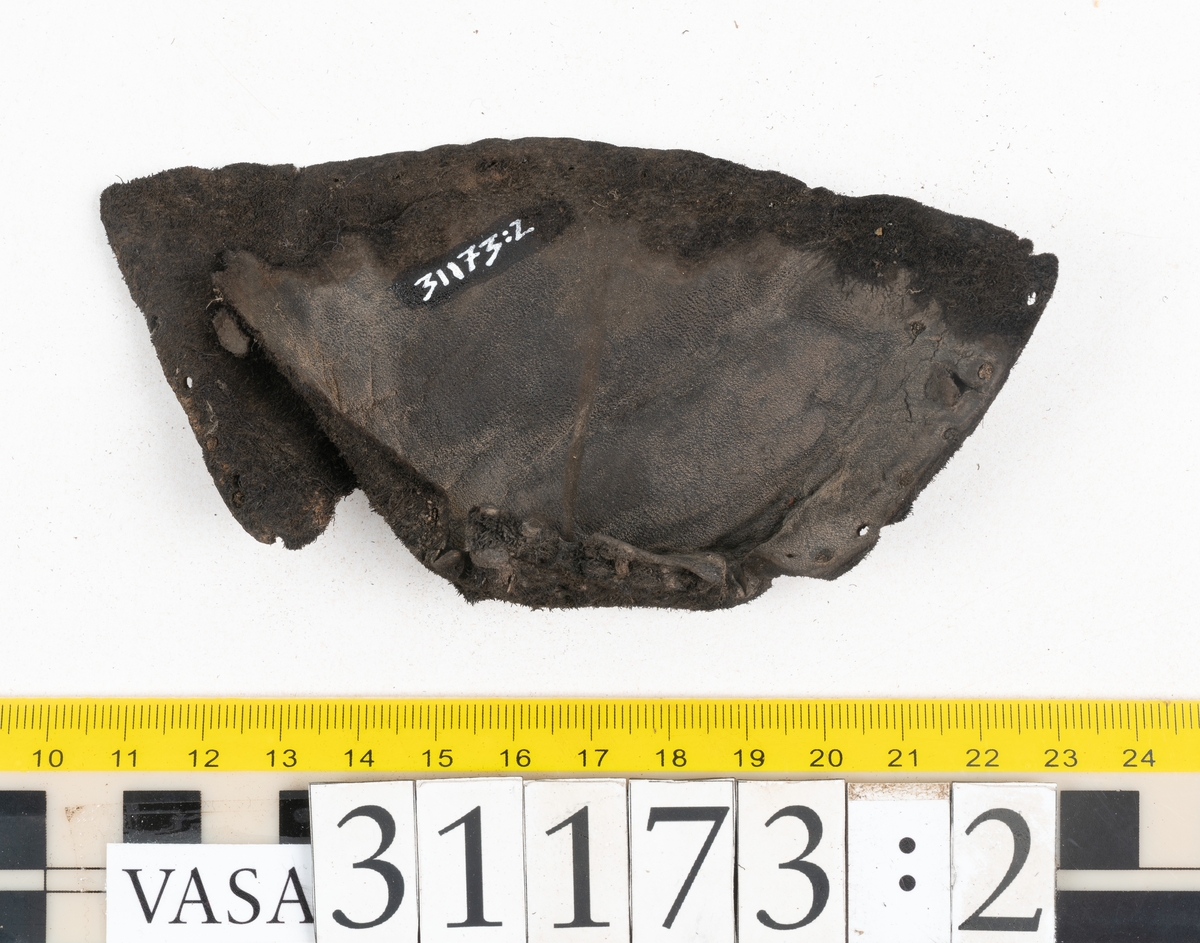 Dokumentation 1998:
Fem delar av överdelen till en slejfsko.
Ett ovanläder med bred och kantigt skuren plös, fyndnummer 31173. Längs med ovanlädrets ena sida och tvärs över tåpartiet löper stygnshål. Längs med ytterkanterna löper hål efter träpligg och stygn. Ovanlädrets främre parti och plös är något fragmentarsika. Lädret är kraftigt med fläckvisa, rostfärgade utfällningar.
En skuren läderremsa, fyndnummer 31173. Remsan har suttit fästad längs ovanlädrets ena sida. Längs med remsans ytterkanter löper hål efter stygn och träpligg.
Två stycken sidostycken med slejf. Sidostyckena har slutit om hälpartiet och fästats samman med en söm mitt bak på skon. Det vänsta sidostycket, fyndnummer 31173:1, är det bäst bevarade. I slejfänden finns ett urtag, troligtvis ett knapphål. Längs med ytterkanterna löper hål efter stygn. Längs den nedre kanten löper hål efter träpligg. Det högra sidostyckets nedre del samt slejfände är fragmentarisk. Lädret är kraftigt och relativt välbevarat.
En förstärkning, fyndnummer 31173:2. Troligtvis har lädret suttit fästat på ovanlädret och förstärkt tåpartiet. Lädret är kraftigt.

Dokumentation 2022:
Del av ovanläder. Framstycke till en sluten sko. Skapades på en rak läst och bars på vänster fot. Inga dekorationer. Fyndnummer 31173:1 är skons bakkappa och den har skador som liknar de från fyndnummer 09806. Fyndnummer 31173:3 är skons sidofoder. Ovanlädrets framstycke och bakkappan saknar vissa fragment och det finns tecken på förstärkningar. Ovanlädrets framstycke har haft förstärkningar på sidans insida och på tån, men de saknas idag. 
För mer information, se Länkade filer: Uppritning

Text in english:
These are a vamp and a quarter of a shoe, made of leather, made on a straight last and worn on the left foot, with no decorative features. 31173:1 represents the quarter and has suffered damage similar to 09805, 31173:3 represents the side lining. There are missing fragments from the vamp and the quarter and there are signs of reinforcements. The vamp had internal reinforcement (missing) only on its lateral side and at the toe.
For more information, go to Länkade filer: Uppritning