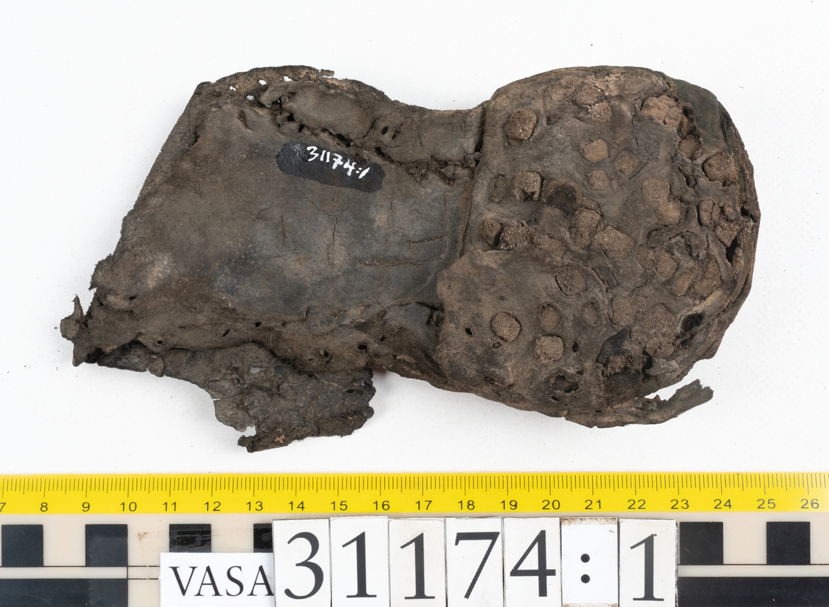 Delar av skobotten.
En sula med kvarsittande del av klacken. Sulan ligger vikt samt är delvis fragmentarisk. Längs med ytterkanterna löper hål efter stygn. Klacken består av fyra klacklappar. Två klacklappar är mycket fragmentariska. Klacken har kvarsittande tråd och träpligg.
En sula. Längs med ytterkanterna löper hål efter träpligg och stygn. Tåpartiet är något fragmentariskt. Lädret är mycket kraftigt.
En klacklapp. Klacklappen är något hästskoformad. På klacklappen syns stora hål efter träpligg.