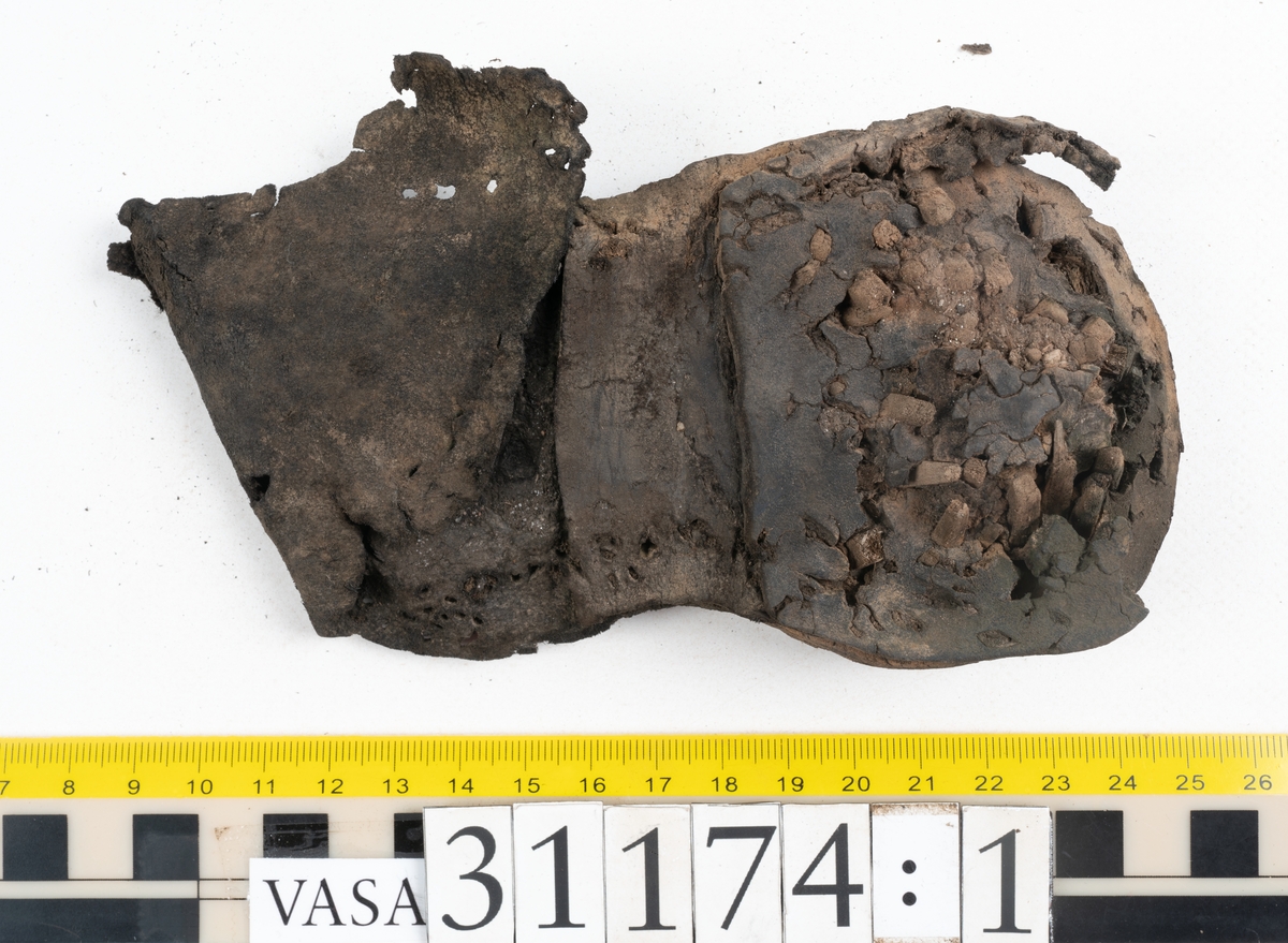 Delar av skobotten.
En sula med kvarsittande del av klacken. Sulan ligger vikt samt är delvis fragmentarisk. Längs med ytterkanterna löper hål efter stygn. Klacken består av fyra klacklappar. Två klacklappar är mycket fragmentariska. Klacken har kvarsittande tråd och träpligg.
En sula. Längs med ytterkanterna löper hål efter träpligg och stygn. Tåpartiet är något fragmentariskt. Lädret är mycket kraftigt.
En klacklapp. Klacklappen är något hästskoformad. På klacklappen syns stora hål efter träpligg.