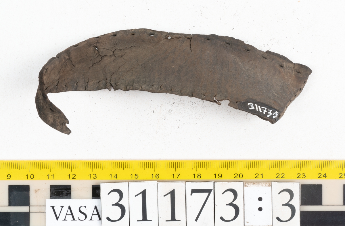 Dokumentation 1998:
Fem delar av överdelen till en slejfsko.
Ett ovanläder med bred och kantigt skuren plös, fyndnummer 31173. Längs med ovanlädrets ena sida och tvärs över tåpartiet löper stygnshål. Längs med ytterkanterna löper hål efter träpligg och stygn. Ovanlädrets främre parti och plös är något fragmentarsika. Lädret är kraftigt med fläckvisa, rostfärgade utfällningar.
En skuren läderremsa, fyndnummer 31173. Remsan har suttit fästad längs ovanlädrets ena sida. Längs med remsans ytterkanter löper hål efter stygn och träpligg.
Två stycken sidostycken med slejf. Sidostyckena har slutit om hälpartiet och fästats samman med en söm mitt bak på skon. Det vänsta sidostycket, fyndnummer 31173:1, är det bäst bevarade. I slejfänden finns ett urtag, troligtvis ett knapphål. Längs med ytterkanterna löper hål efter stygn. Längs den nedre kanten löper hål efter träpligg. Det högra sidostyckets nedre del samt slejfände är fragmentarisk. Lädret är kraftigt och relativt välbevarat.
En förstärkning, fyndnummer 31173:2. Troligtvis har lädret suttit fästat på ovanlädret och förstärkt tåpartiet. Lädret är kraftigt.

Dokumentation 2022:
Del av ovanläder. Framstycke till en sluten sko. Skapades på en rak läst och bars på vänster fot. Inga dekorationer. Fyndnummer 31173:1 är skons bakkappa och den har skador som liknar de från fyndnummer 09806. Fyndnummer 31173:3 är skons sidofoder. Ovanlädrets framstycke och bakkappan saknar vissa fragment och det finns tecken på förstärkningar. Ovanlädrets framstycke har haft förstärkningar på sidans insida och på tån, men de saknas idag. 
För mer information, se Länkade filer: Uppritning

Text in english:
These are a vamp and a quarter of a shoe, made of leather, made on a straight last and worn on the left foot, with no decorative features. 31173:1 represents the quarter and has suffered damage similar to 09805, 31173:3 represents the side lining. There are missing fragments from the vamp and the quarter and there are signs of reinforcements. The vamp had internal reinforcement (missing) only on its lateral side and at the toe.
For more information, go to Länkade filer: Uppritning