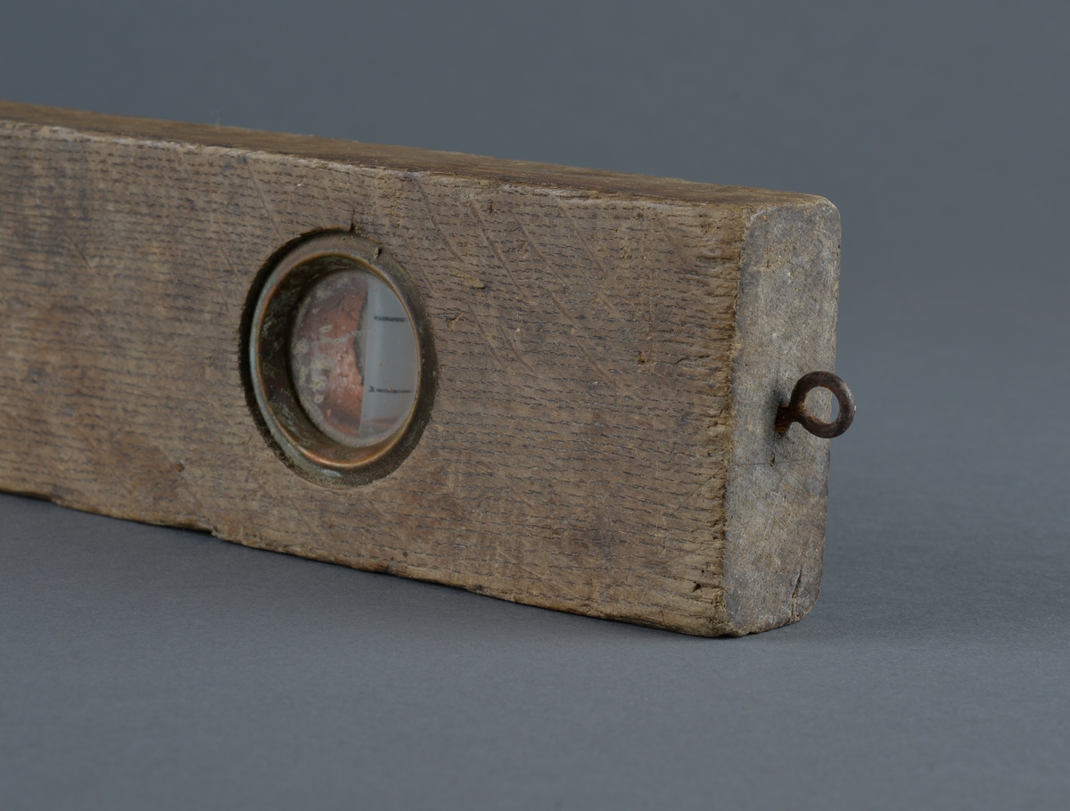 Rektangulær trevater med metallinnfellinger for å måle at arbeidet er vannrett
Ovalt utfreset spor på vaterens midtdel
Liten øyekrok, antatt for oppheng i ene tverrkanten.