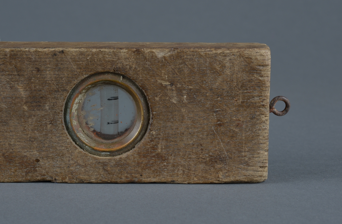 Rektangulær trevater med metallinnfellinger for å måle at arbeidet er vannrett
Ovalt utfreset spor på vaterens midtdel
Liten øyekrok, antatt for oppheng i ene tverrkanten.