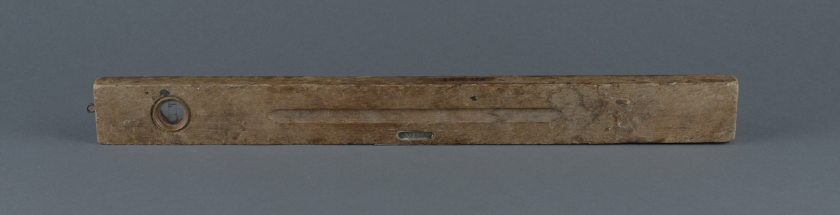 Rektangulær trevater med metallinnfellinger for å måle at arbeidet er vannrett
Ovalt utfreset spor på vaterens midtdel
Liten øyekrok, antatt for oppheng i ene tverrkanten.