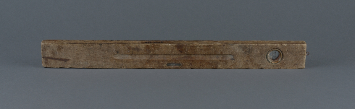 Rektangulær trevater med metallinnfellinger for å måle at arbeidet er vannrett
Ovalt utfreset spor på vaterens midtdel
Liten øyekrok, antatt for oppheng i ene tverrkanten.