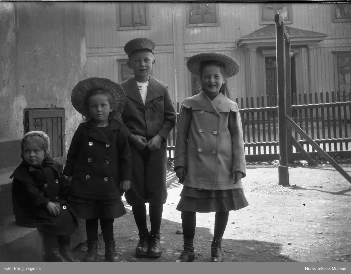 Barn, tre piker og en gutt i sin fineste utestas fotografert i haven oppstilt foran stakittgjerde : muligens Ægidius Ellings døtre i forgrunnen