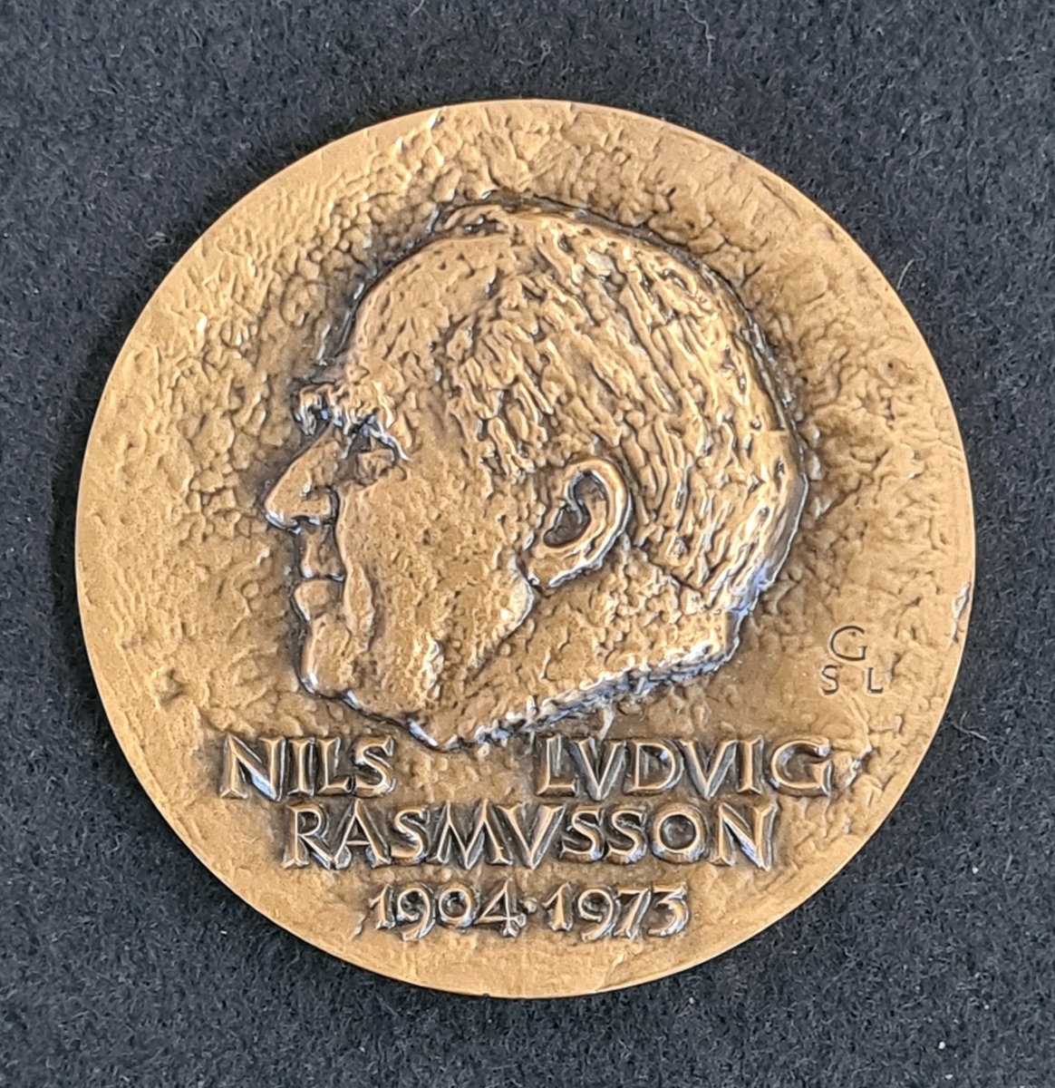Minnesmedalj i brons. Sid 1: Porträtt i relief och texten: Nils Ludvig Rassmusson 1904-1973.
Sid 2: En pil och texten ''Viam quaerit, viam monstrat = Han utforskar vägen, han visar den''
