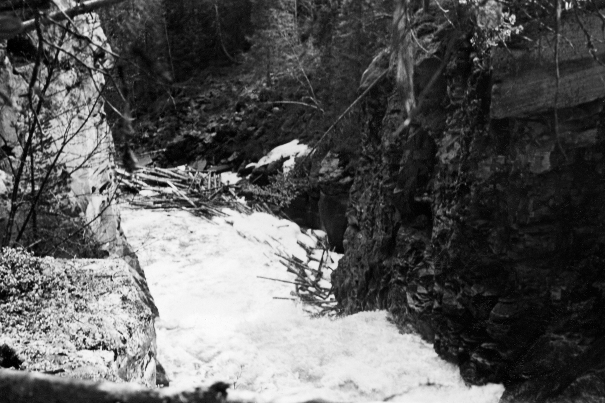 Det nedre fallet i elva Hira i Stor-Elvdal.  Fotografiet er tatt i mai 1958, da det var forholdsvis mye vann i fossen.  I det nedre Hirfallet renner elva mellom to forholdsvis steile bergflater, hvor det åpenbart var vanskelig for tømmerfløterne å komme til dersom virket satte seg fast, noe vi ser tendenser til på høyre side av elveløpet.  Strid strøm og mye stein slet ofte hardt på tømmeret her.  Åforbedringsarbeider reduserte etter hvert dette problemet noe, men greide aldri å eliminere det. 