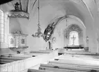 Interiör från Kaga kyrka 1903, ännu med den gamla bänkinredningen som kom att förändras vid 1907 års restaurering. I senare tid har även väggarnas och valvbågarnas medeltida bemålning framtagits. En mindre förändring är placeringen av huvudbanéret till minne av Nathanael Gyllenram som flyttats till kyrkans södra vägg. Den nätta predikstol är dock oförändrad, utförd av snickarmästare Niclas Österbom 1747.