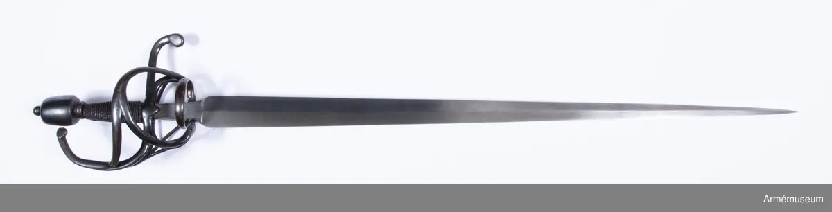 Den tveeggade klingan är upptill rätt bred samt avsmalnar långsamt och likformigt mot udden så att den får formen av en långdragen triangel. På vardera flatsidan har klingan längsgående rygg, och upptill en cirka 65 mm lång ansats, som har plana flatsidor och svagt kullriga eggsidor. Vid klingbasen är ansatsen 28 mm men vid fästet 19 mm bred. Längs var och en av ansatsens långkanter går på flatsidorna en ingraverad rand. På var och en av ansatsens flatsidor finns en krönt stämpel med bokstaven S över bokstaven T, samt på innersidan dessutom bokstäverna H Z under en krona, vilket lär betyda Hauptzeughaus. Fästet är av svärtat järn. Knappen har närmast formen av en långdragen, stympad kon med kullrig översida och med rygg längs var eggsida, så att den får spetsovalt tvärsnitt.  Nitknappen är rätt hög och avskiljes genom en horisontal fals  från knappen. Knappens hals är kort och kullrig samt  avskiljes även den genom en horisontal fals från knappen. På yttersidan av knapphalsens underkant finns fyra inhuggna streck.

Träkaveln är närmast spolformig, men betydligt bredare vid korset än vid knappen. Flatsidorna är kullriga, men längs vardera eggsidan går en försänkt rand. Nedtill har kaveln krans av snodd järntråd, men den övre kransen är förkommen. Kavellindningen består av en rätt grov, överspunnen järntråd samt av en höger- och en vänstersnodd järntråd, vardera hoptvinnad av två parter. Parerstången har spetsovalt tvärsnitt samt vid korset på var sida en trekantig, nedåtvänd flik. Baktill är parerstången nedböjd och avslutas med en skivformig utsvällning, som är svängd litet åt yttersidan. Framtill övergår parerstången bågformigt i handbygeln, vilken upptill avslutas med en flat skiva, vars kant står några millimeter framför knappen. Från korset utgår vid var och en av ansatsens eggsidor en stor,  nedåtriktad fingerhake. De båda fingerhakarnas nedre ändar förenas på yttersidan med en horisontal bygel. På samma sida utgår även en från fingerhakarnas nedre ändar en snett uppåtriktad, i ca 45 graders vinkel ställd stor parerbygel, vars övre kant står i jämnhöjd med kavelns nedre del. Från  den hösta punkten på denna bygel går en spång till handbygelns mitt. På innersidan går en nedtill tregrenigt S-formig gaffelspång från handbygelns mitt till fingerhakarnas nedre ändar. Gaffelspångens olika delar har cirkelrunt tvärsnitt, men yttersidans byglar och spång har kullrig utsida och flat insida.