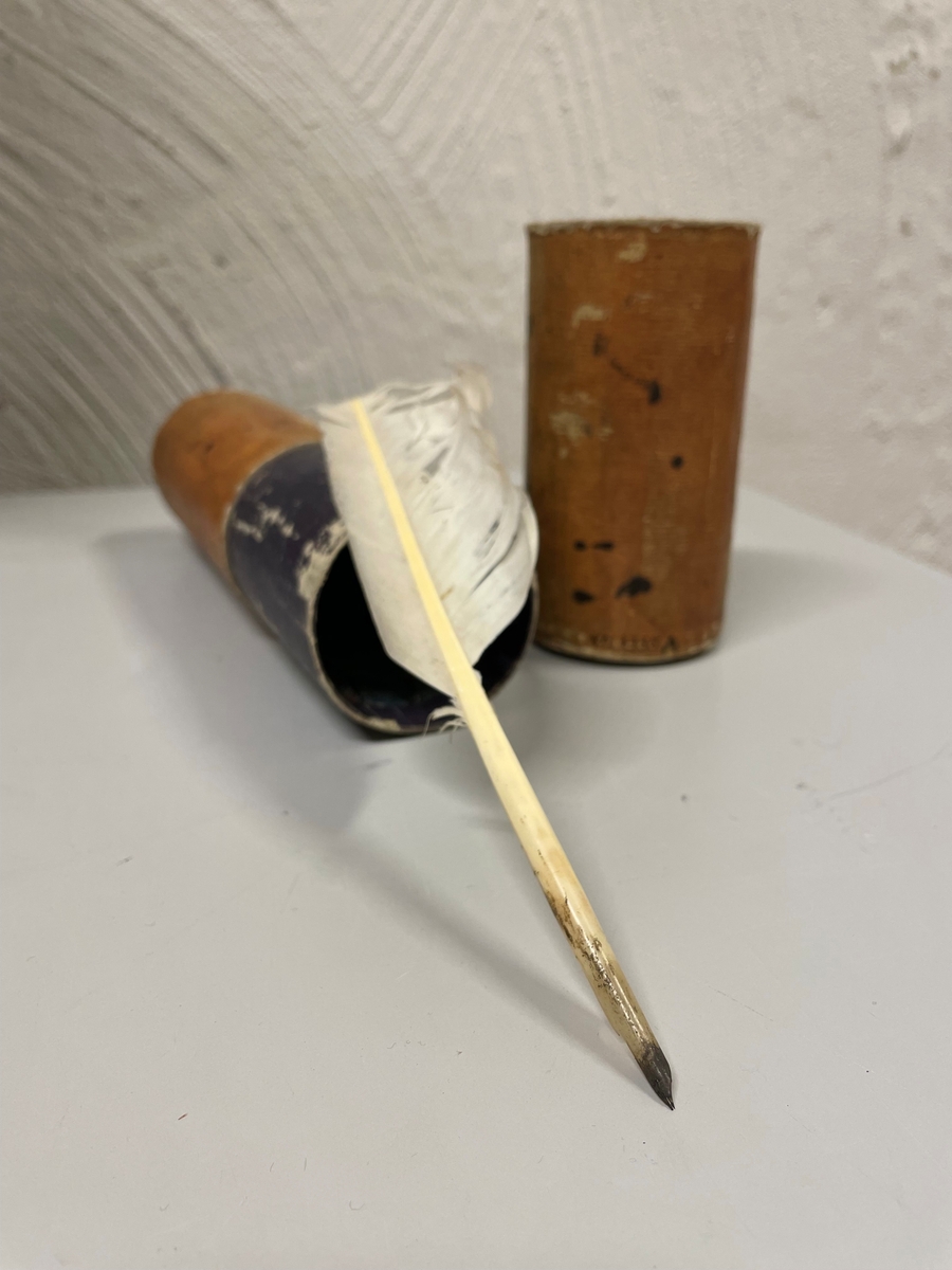 Cylinderformat fodral av papp, klädd med gulbrunt papper. Kanterna vid öppningen har förgyllda bårder. Ena kortänden har initialerna E. T. i förgyllning. Inuti ligger en kort fjäderpenna.