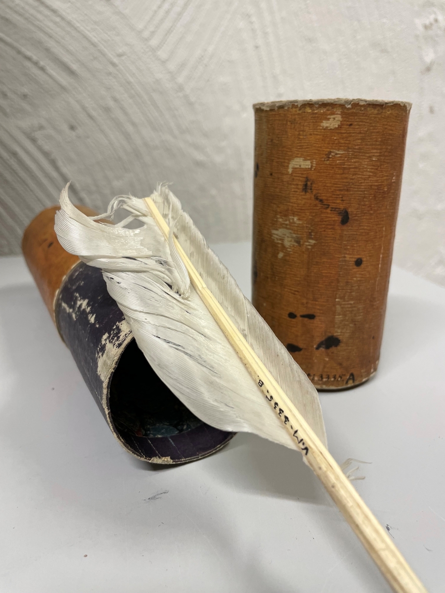 Cylinderformat fodral av papp, klädd med gulbrunt papper. Kanterna vid öppningen har förgyllda bårder. Ena kortänden har initialerna E. T. i förgyllning. Inuti ligger en kort fjäderpenna.