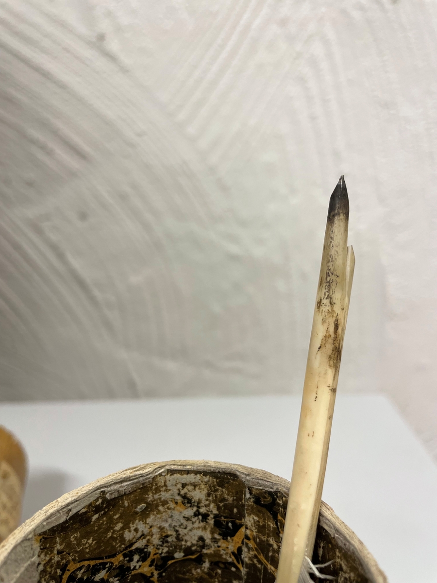 Cylinderformat fodral av papp, klädd med gulbrunt papper. Kanterna vid öppningen har förgyllda bårder. Ena kortänden har initialerna E. T. i förgyllning. Inuti ligger en kort fjäderpenna.