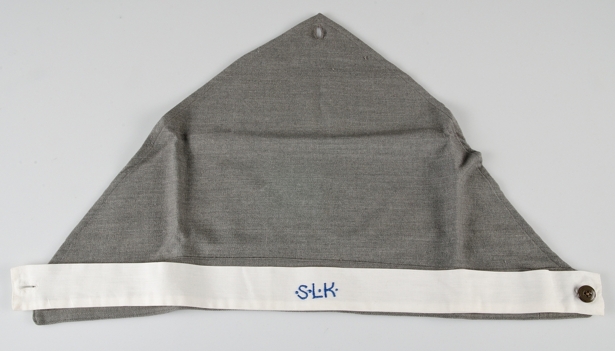 Klänning av grått ylletyg. Knälång klänning med isydd lång ärm. Kjolen har två nedsydda vecka fram och två fickor och ett veck bak. Knäppning från krage till midja med tio grå knappar.Knappar i handled.  Påsydda axelklaffar. Manchetter i vitt, löstagbara, påknäppt vit krage av konstsilke.Till klänningen hör skärp med knappar och knapphål och huvudbonad av samma tyg, snibb med knappar bak, påknäppt itt band fram med blått broderi: S.L.K (Sveriges lottakår). Mössan är märkt med samma UM nummer som klänningen.  Klänningen har löstagbara märken på axelklaffarna : 2. På bröstet  flera märken se UM 25.916. Ärmlängd 48 cm, axelbredd 48 cm, vidd 200 cm.