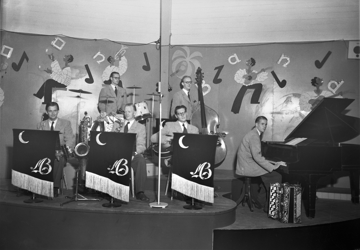 Orkestern Moon band spelar i Nöjesparken i september 1943. Första bilden visar sexmannabandet på scen och på bild 2 står de samlade nedanför scenen. De har med en nalle som mascot. På väggen en målad dekor med noter och musiker. (Se även bild GB2_4017)

Moon band bildades 1932-33 av bröderna Janne och Olle Olausson, men ombildades omkring 1940 med följande sättning: Sten-Gunnar Svensson, trummor; Rune Svensson, dragspel (senare även piano, som på bilden); Sigge Börjesson, trumpet; Yngve Persson, saxofon; Bertil "Lången" Olsson, gitarr; Eric Nyholm, piano (ersattes av Rune). Gunnar Karlsson tillkom på kontrabas.