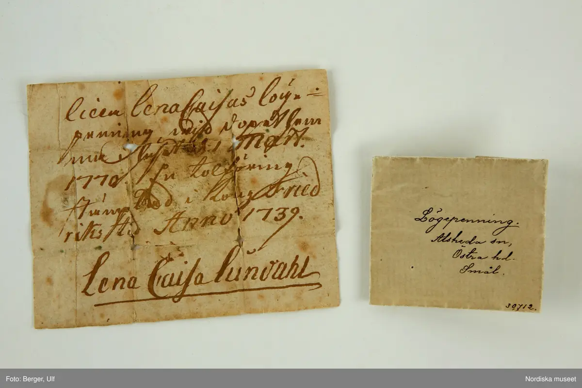 Huvudliggaren:
"'Lögepenning' fr. Alseda sn, Östra hd. Småland. Märkt 'IN. DEO. SPES. MEA. 1739.' '10. ÖR. S.M. H.M.' Penningen inlagd i ett papper, å hvilket läses: 'LIna Caisa Lundahl.' G. af fru Maria Kinnvall i Stockh. 26/4 1881. 
Pengen stulen men papperet finns kvar (enl. uppgift 1943) 1978-01-11/MP.
"Inom Småland och måhända äfven inom andra delar af vårt land var det förr brukligt, att, då ett nyfödt barn badades första gången, lades ett mynt i badet. Myntet, som kallades lögepenning förvarades af barnets moder, hvilken försåg det med ett omslag, hvarå antecknades barnets namn, födelseår och dag, tiden, då myntet var pregladt, m.m., samt moderns namn som underskrift. Sedan barnet växt upp, blef detta rätta egaren till myntet, som förvarades och gick i arf från led till led inom slägten." "

Bilaga:
Inget utöver huvudliggaren

Omslagets påskrift:
""Lilla Lena Caisas lögepenning wid dopet hemma i huset d. 1 Mart. 1770. En tolföring stämplad i Kong Friedriks tid. Anno 1739. Lena Caisa Lundahl."
Lena Kättström Höök 2014-10-07
