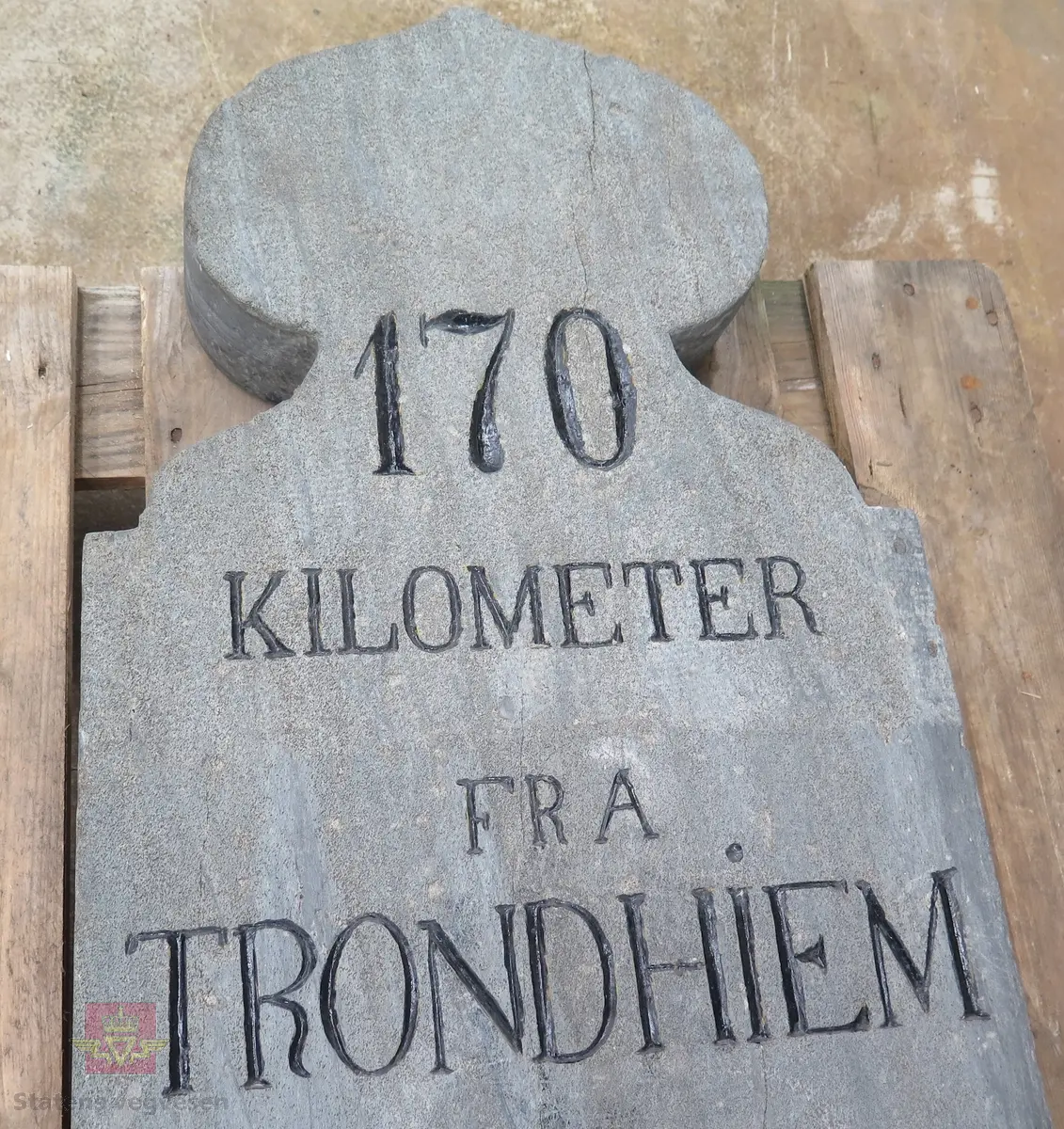 Rektangulær massiv stein, formet som en løk i toppen. Grå. Har teksten: 170 KILOMETER FRA TRONDHIEM. Teksten er preget inn i steinen og malt svart. Steinen ser ut til å være skjøtet sammen av to deler. Bærer preg av oppussing.