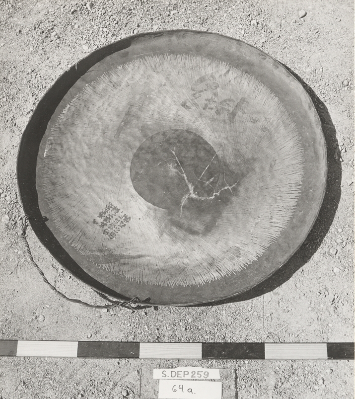 Uthamrad, cirkelrund, svagt buktig med nedhamrad kant. Lagad med två tennlödda mässingsplåtar. Upphängningsanordning av wire. Två träklubbor med klotformiga slag. Kinesiska tecken på baksidan.