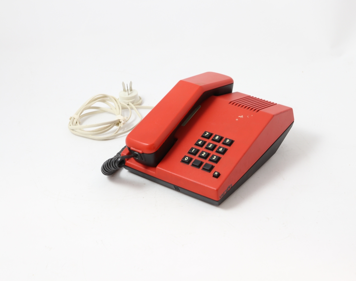 Rød telefon med tastatur. Telefonen er rektangulært formet med skråstilt front med tastatur, og har en fordypning for plassering av tale-/hørerør. Ledningsdel med egen telekontakt. På undersiden to reguleringsknapper: "tone". På overdeksel høyttaler/lyd-forsterker "vilum"