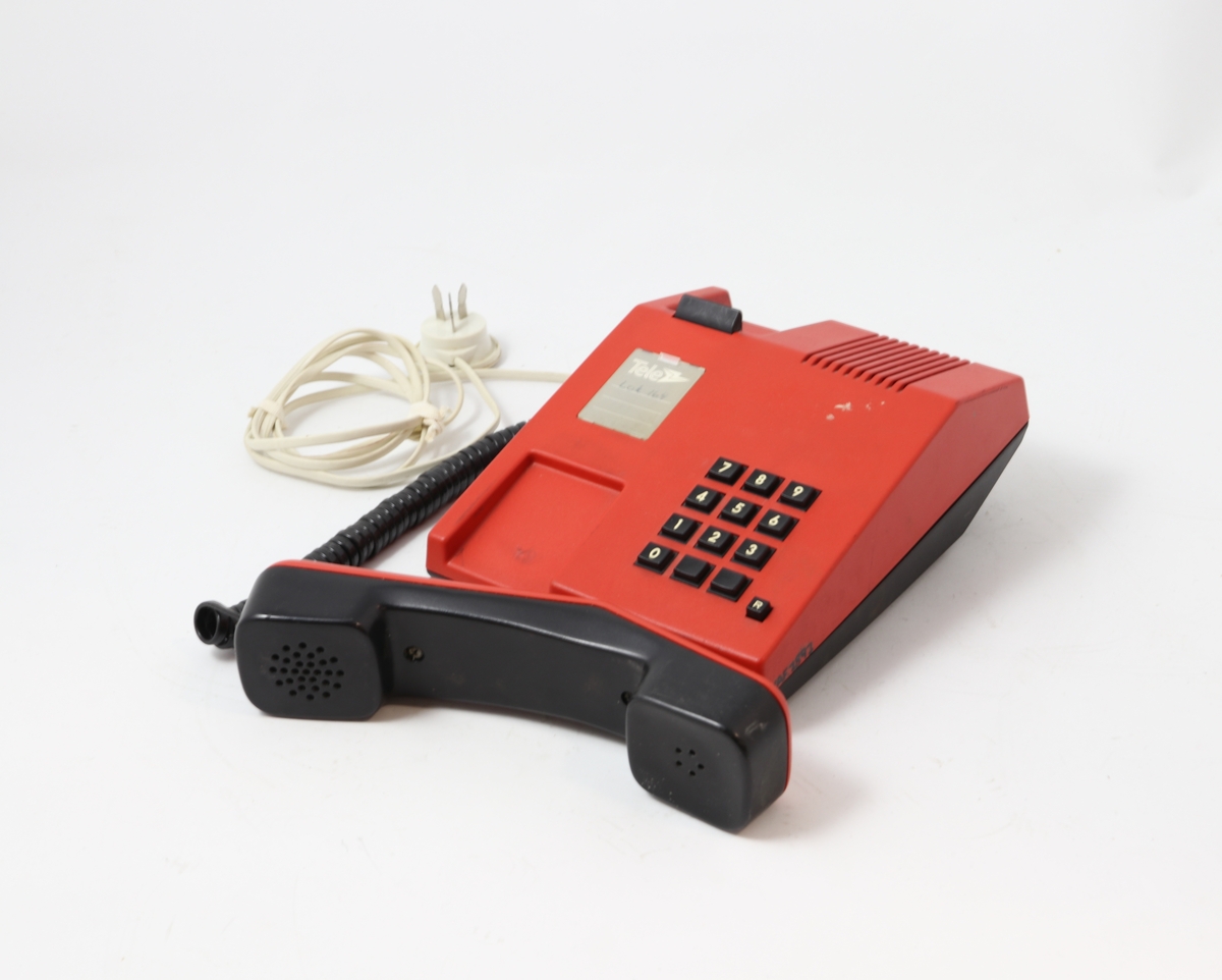 Rød telefon med tastatur. Telefonen er rektangulært formet med skråstilt front med tastatur, og har en fordypning for plassering av tale-/hørerør. Ledningsdel med egen telekontakt. På undersiden to reguleringsknapper: "tone". På overdeksel høyttaler/lyd-forsterker "vilum"