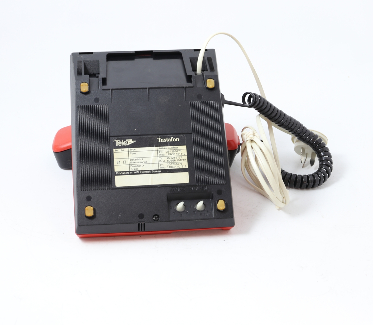 Rød telefon med tastatur. Telefonen er rektangulært formet med skråstilt front med tastatur, og har en fordypning for plassering av tale-/hørerør. Ledningsdel med egen telekontakt. På undersiden to reguleringsknapper: "tone". På overdeksel høyttaler/lyd-forsterker "vilum"