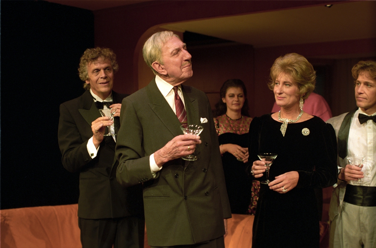 Scene fra Nationaltheaterets oppsetning av Alan Ayckbourns "Monki Bisniss". Desmond, Ken Ayres, Yvonne og Roy står sammen med cocktailglass i hendene. Bak sees Anita. Forestillingen hadde premiere 8. september 1989. Toralv Maurstad hadde regi og medvirkende var blant annet Tor Stokke som Jack, Kari Simonsen som Poppy og Leif Juster som Ken Ayres. 