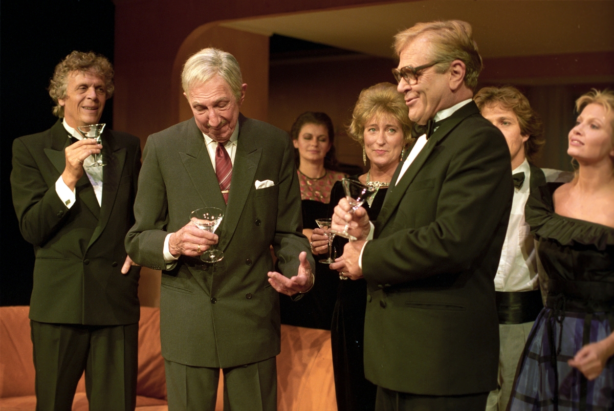Scene fra Nationaltheaterets oppsetning av Alan Ayckbourns "Monki Bisniss". Desmond, Ken Ayres, Yvonne, Jack og Tina snakker sammen med cocktailglass i hendene. Forestillingen hadde premiere 8. september 1989. Toralv Maurstad hadde regi og medvirkende var blant annet Tor Stokke som Jack, Kari Simonsen som Poppy og Leif Juster som Ken Ayres. 