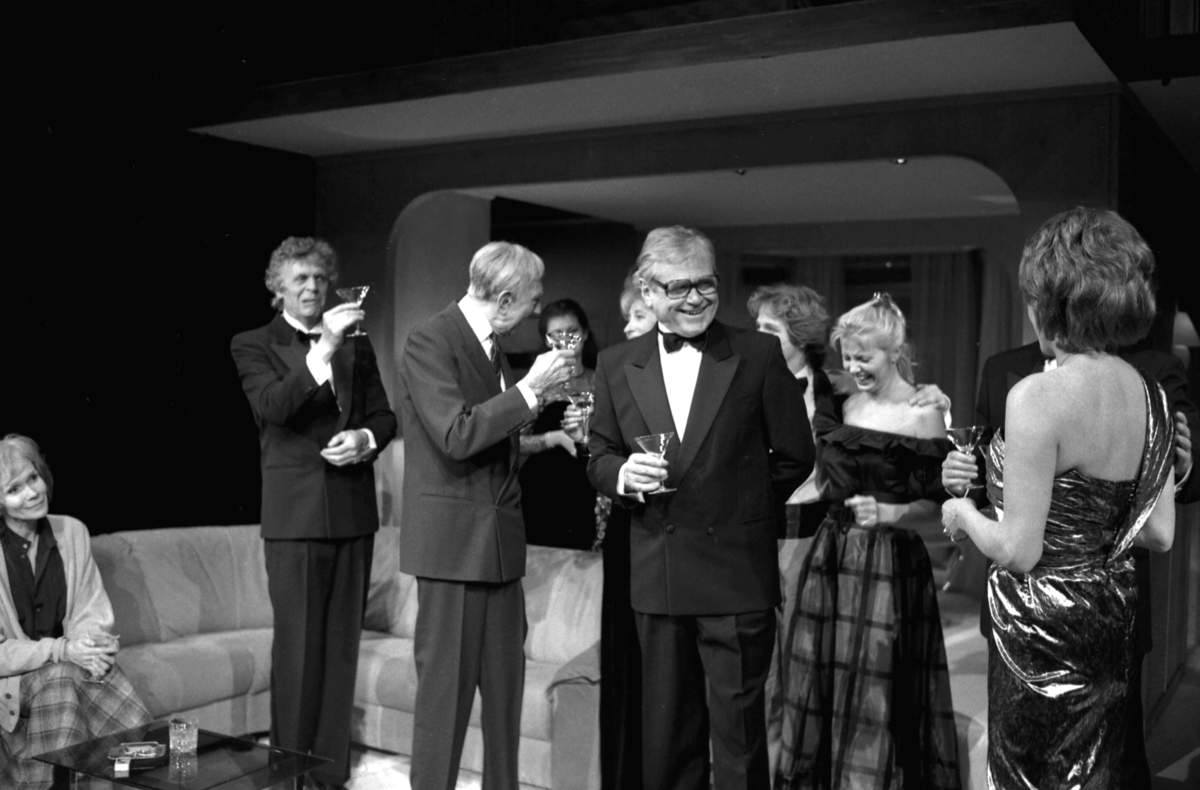 Scene fra Nationaltheaterets oppsetning av Alan Ayckbourns "Monki Bisniss". Ni kvinner og menn kledd for fest står i en gruppe, der de prater og drikker. Forestillingen hadde premiere 8. september 1989. Toralv Maurstad hadde regi og medvirkende var blant annet Tor Stokke som Jack, Kari Simonsen som Poppy og Leif Juster som Ken Ayres.  
