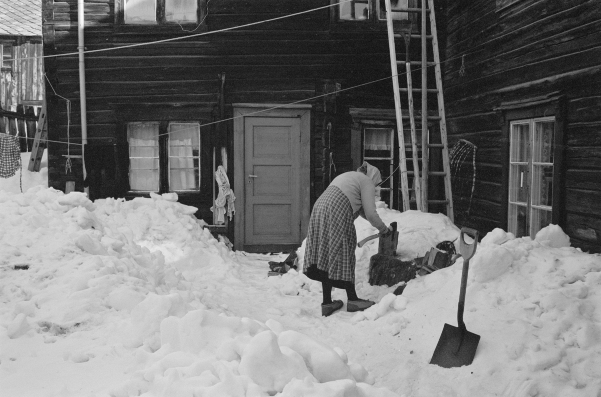 En kvinne hogger ved i et gårdsrom på Røros.