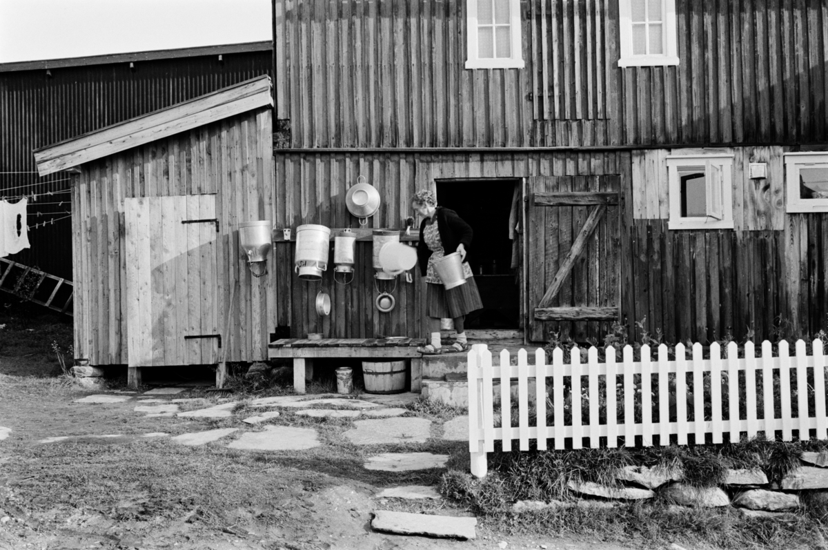 En kvinne står med melkespann i et gårdsrom på Røros.