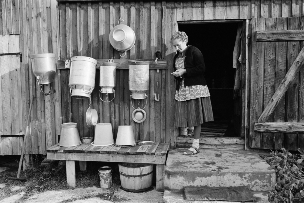 En kvinne står med melkespann i et gårdsrom på Røros.