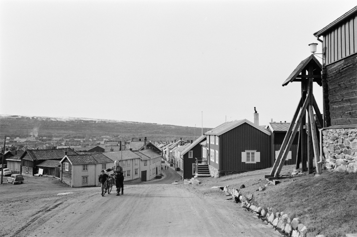 En kvinne og et barn med sykkel går i en gate på Røros.