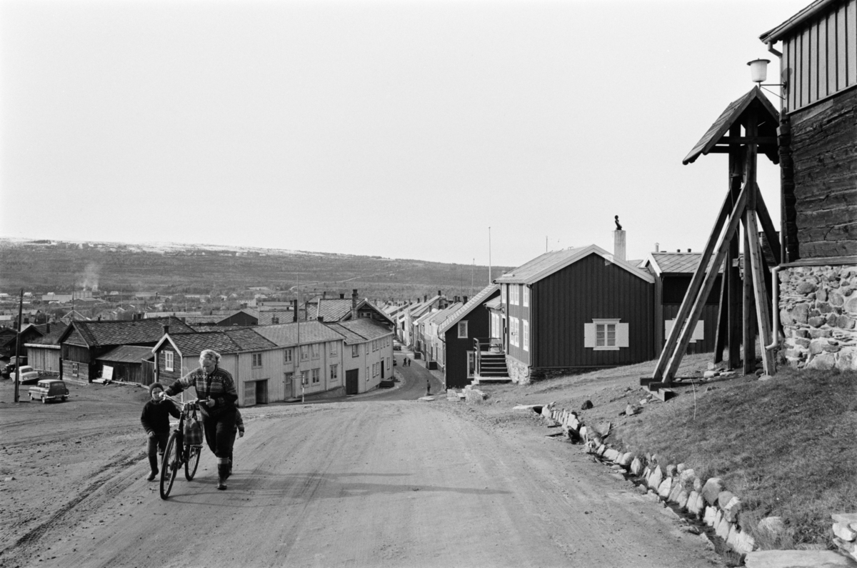 En kvinne og et barn med sykkel går i en gate på Røros.