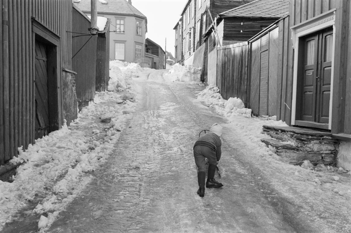 Et barn leker med en kjelke i en gate på Røros.