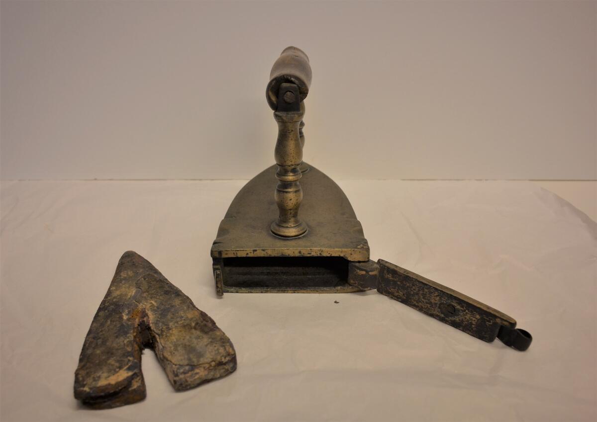 Strykjärn av malm, med järnlod och dörr med hasp på baksidan. Handtagsgrepp av trä.  Ristad på sidorna: H.H.N. E:E:S 1787. Gåva: Fru häradshövding Grufman, Sthlm 1960, samlingen har tillhört fadern distriktslantmätaren A.H.L. Andersson, Sollefteå