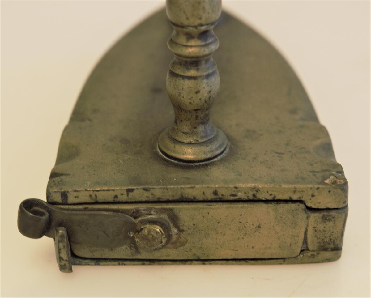 Strykjärn av malm, med järnlod och dörr med hasp på baksidan. Handtagsgrepp av trä.  Ristad på sidorna: H.H.N. E:E:S 1787. Gåva: Fru häradshövding Grufman, Sthlm 1960, samlingen har tillhört fadern distriktslantmätaren A.H.L. Andersson, Sollefteå