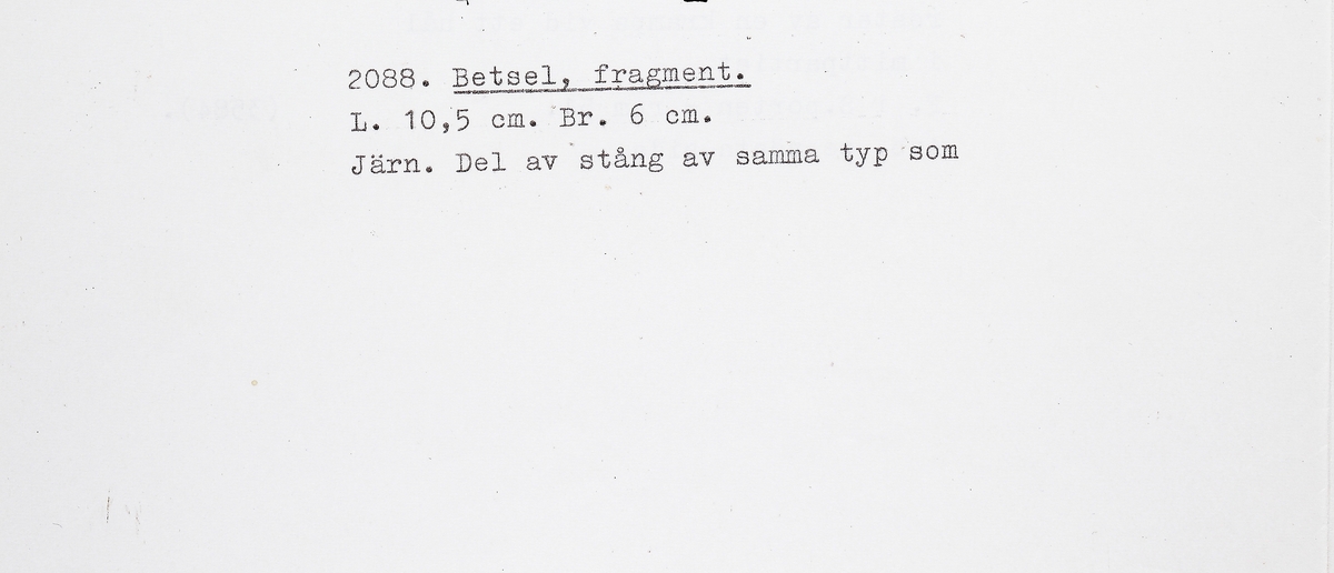 Fragment av stångbetsel till hästträns. Utgör det ena av två par S-formade sidostycken med smalare underskänklar. I underskänkelns spets finns en nit med en ögla som tjänar som axel för en ännu rörlig spiralvriden ten med runda ändplattor. Det S-formade sidstycket är platt och har en urgröpning för bettet som saknas. Även överskänkeln saknas. Samma typ som M 17001: 2087, men något enklare utformning.