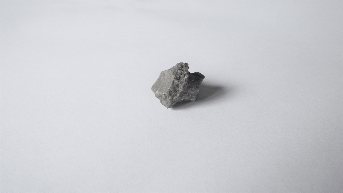 T-formet metallgjenstand med en glatt, buet overflate. På undersiden av buen sees en smalere tapp. Dette er sannsynligvis en del av en gryte der støpetappen fortsatt sitter i. 