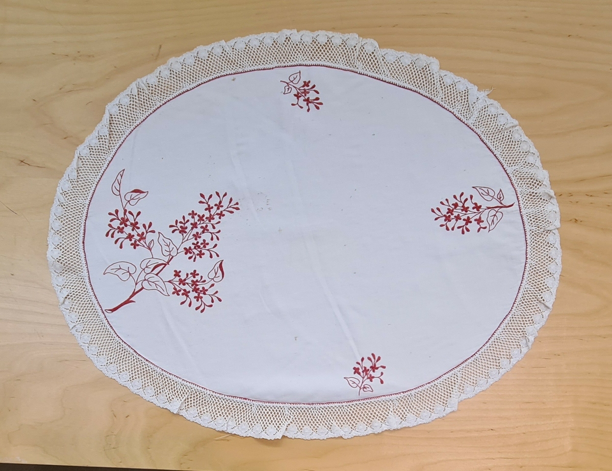 Kypertvävd vit duk med broderi, blombuketter i rött. Spetskantad. Använd av givarens mormor Anna Maria Andersson 1854-1921.