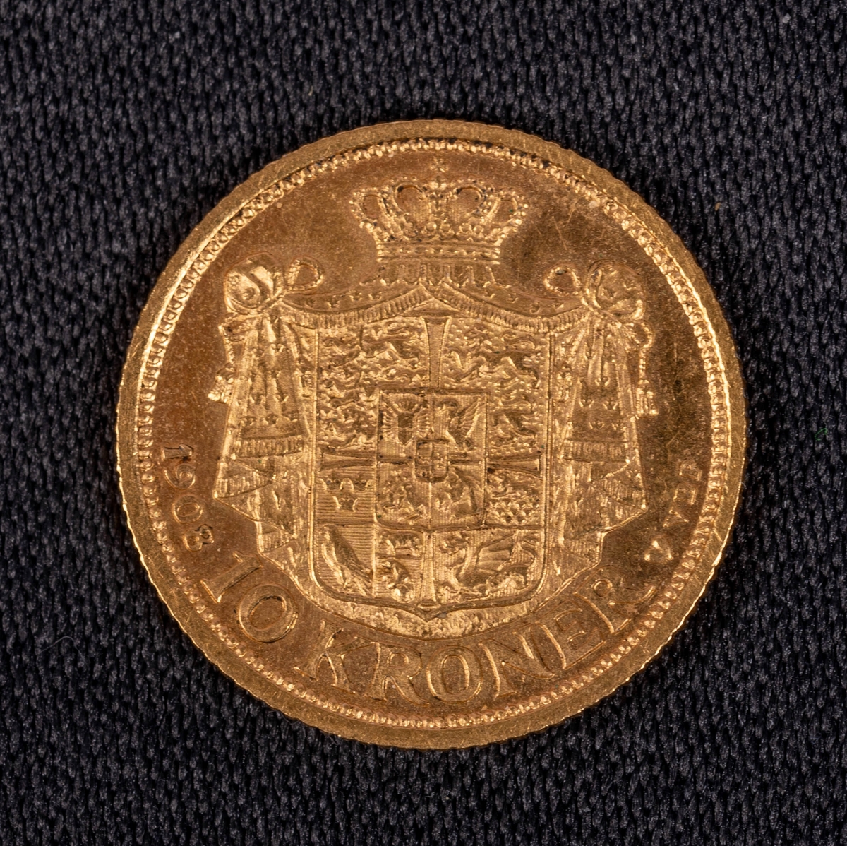 Danskt guldmynt, valör 10 kronor, från 1908. Ena sidan: Riksvapen, text: "1908 10 Kroner vbp". Andra sidan: Manshuvud i profil, text: "Frederik VII Danmarks Konge".