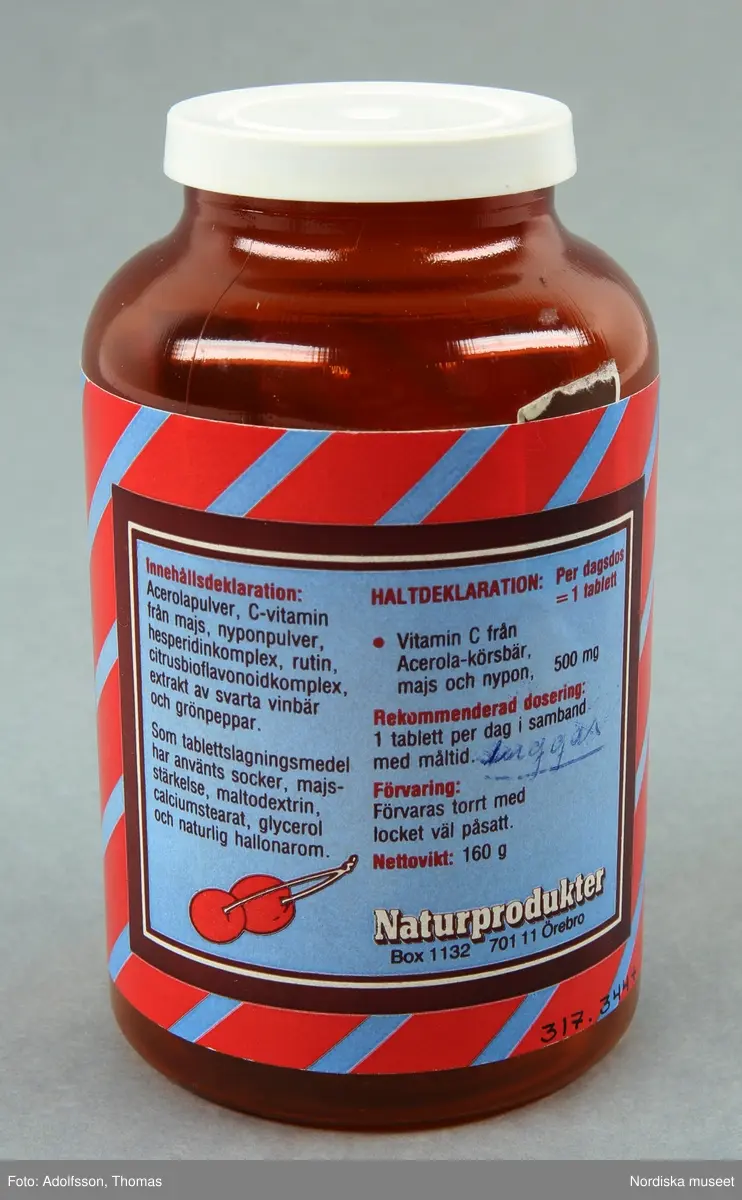 Huvudliggaren:
"Vitaminpillerburk, plast, gjuten. Brun klar cylindrisk, skuldra, kort hals, vitt snäpplock. Blå/röd etikett: Acerola c-vitamin. Tillv Naturprodukter Örebro. Anv Astrid Broman 1990, Ulrikag, Sthlm. H 10,5 Diam 6,5 cm. Gåva 30/10 1991 av Fröken Astrid Broman Ulrikagatan 2, Stockholm."