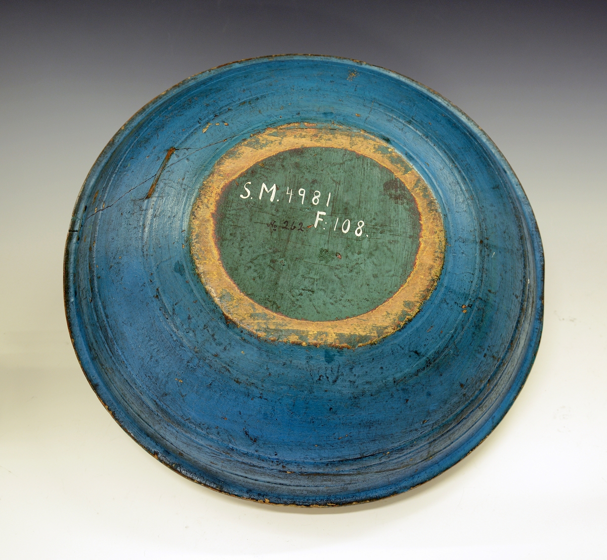 Rosemalt ølbolle. Fra protokollen: Ølbolle, svarvet med sterkt utstaaende ribbe, hvorfra en kant böier ind. Nyere overmaling, utenpaa malt lyseblaa med minjerød kant, hvorpaa indskriften: "Drik min Ven. Jeg dig det Under. Pust imelem og Giv dig stunder. G.G.S. 1868". Indeni er paa gulbrun bund  malt svære roser i c-oplæg og nærmest i Luraasstil; farver: rødbrunt, grønt, blaat, hvitt, gult; sort skrafering. Bollen er kinget.