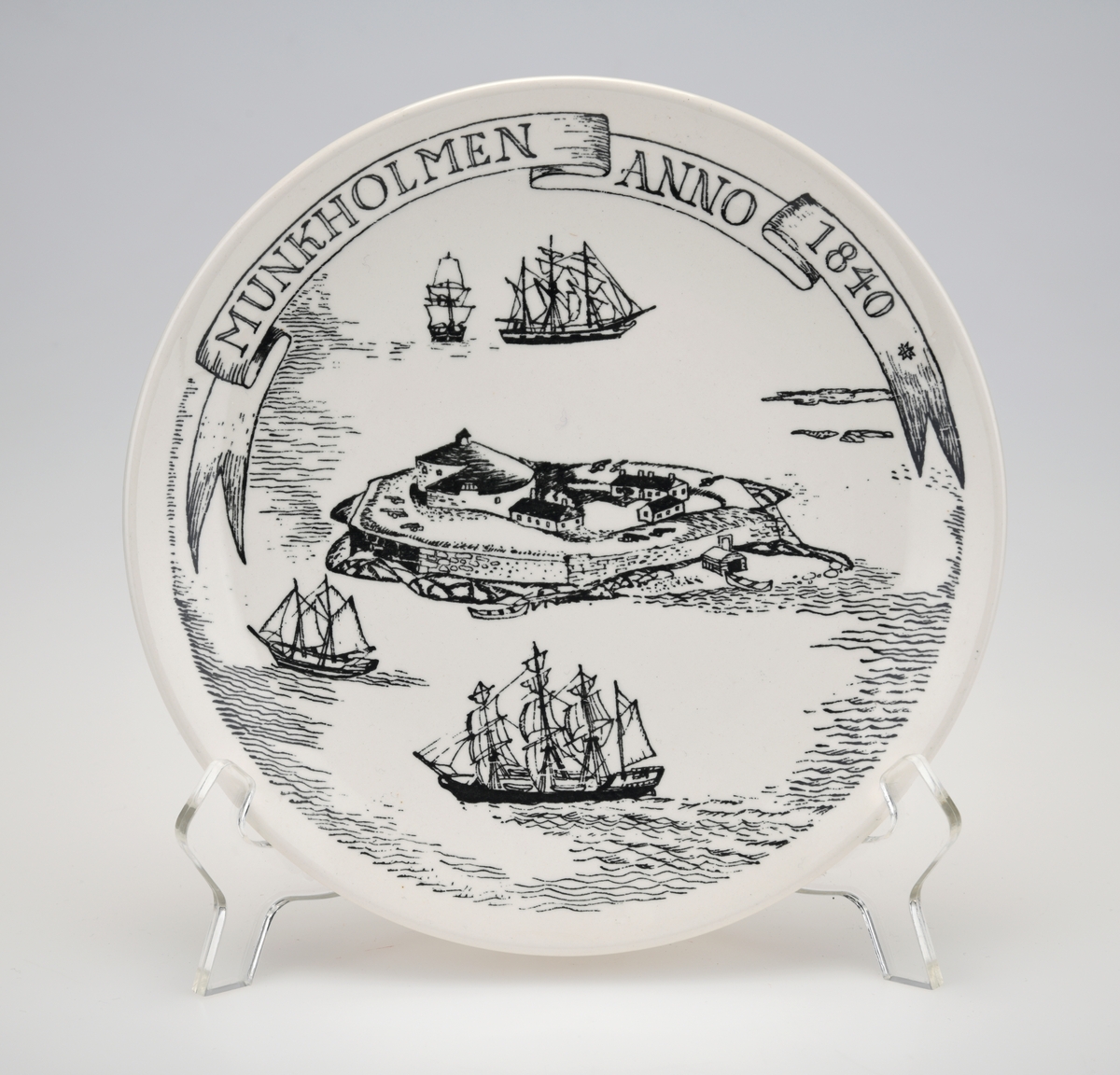 En hvit pyntetallerken med motiv fra Munkholmen anno 1840. Tallerkenen er av flint/steintøy og motivet er trykt på. Øverst på tallerkenen er stedsnavn og årstal. Motivet viser Munkholmen med seilbåter rundt. På baksiden er det hull med itredd hyssing for oppheng på vegg. Det er påført tekst både på for- og bakside, se "Påført tekst/merker".