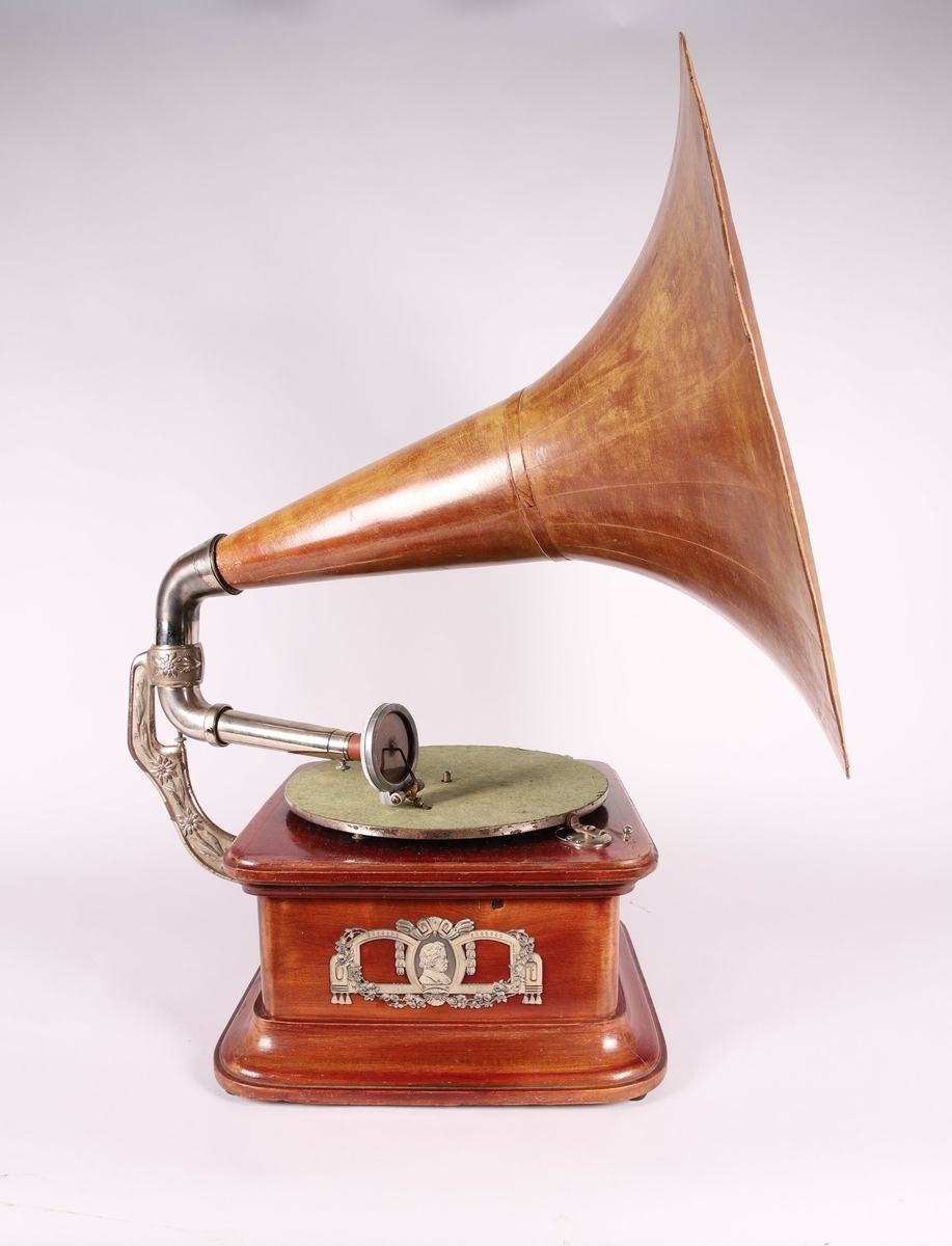 Pathéfon avspiller i treverk med finér. Sveiv på høyreside. Trakt i finér/treverk, med tynt lag av metall mellom lagene. Trakten kan løsnes fra instrumentet.