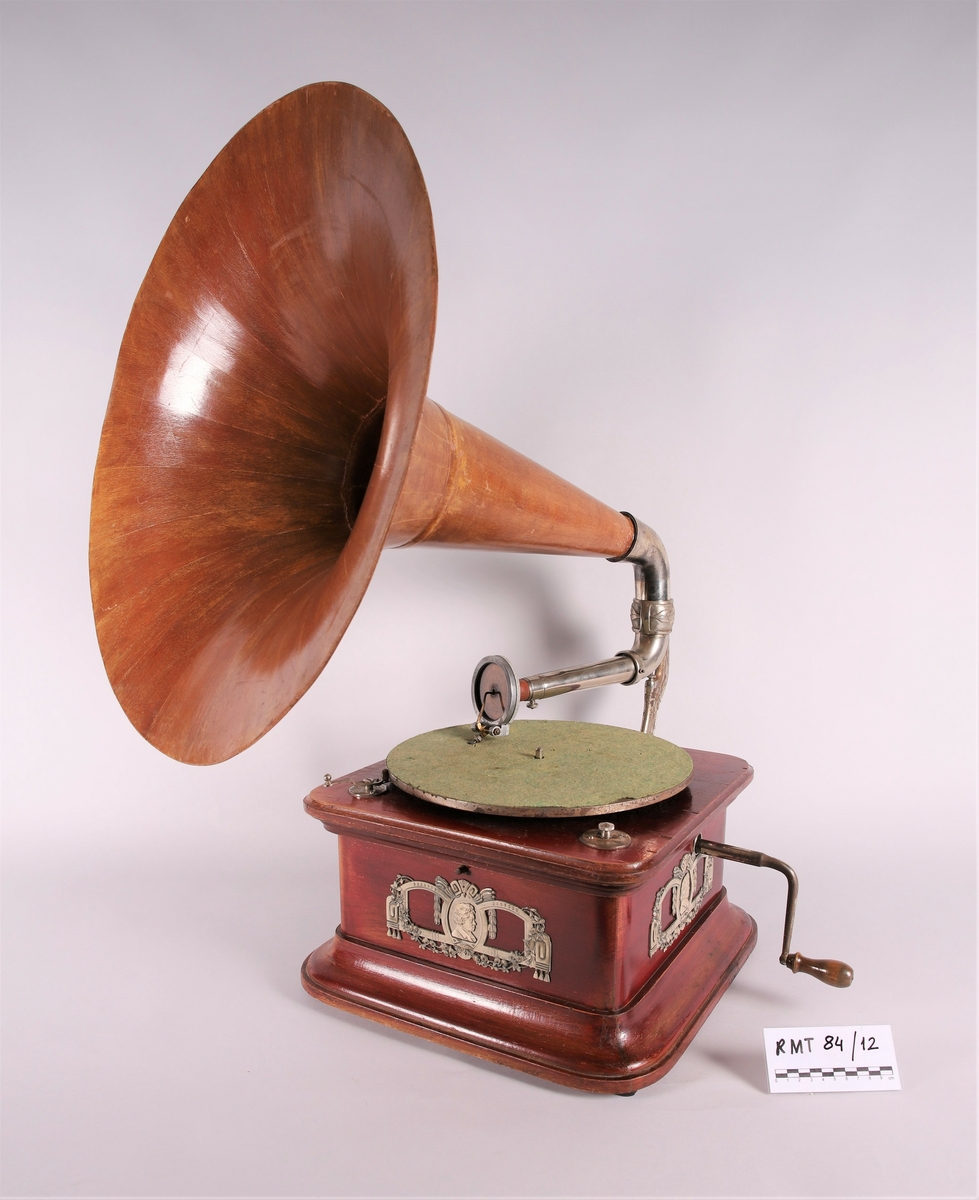 Pathéfon avspiller i treverk med finér. Sveiv på høyreside. Trakt i finér/treverk, med tynt lag av metall mellom lagene. Trakten kan løsnes fra instrumentet.