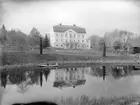 En av tiden medfaren vy mot Kvarns herrgård. Året är 1906 och godset hade nyligen förvärvats av häradshövding Pehr Orre. Huvudbyggnaden var ursprungligen uppförd år 1831 men hade efter en förödande eldsvåda i slutet av 1850-talet byggts upp efter ritningar av den flitigt anlitade herrgårdsarkitekten August Nyström. På Kvarnsån färdas möjligtvis tre av ägarens fyra söner.