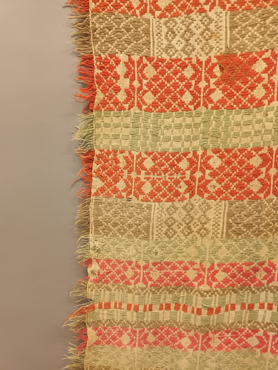 Sauma teppe i ullgarn. Bordar med firkantformer, kryss, åttebladsroser m.m. Teppet er handsauma,brodera med vevsaum på toskaftsbotn i lin. Botn er sauma saman på midten. Teppet har tre små lykker i den eine kortenden. Teppet er noko falma på rettsida, og er noko slite.