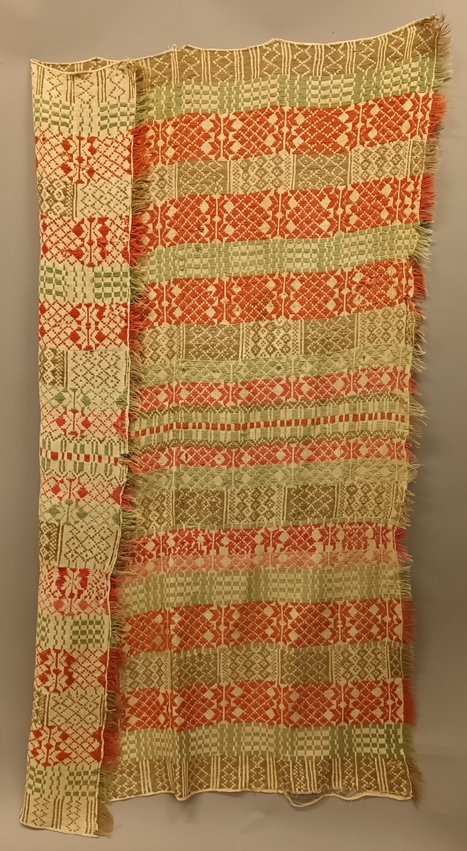 Sauma teppe i ullgarn. Bordar med firkantformer, kryss, åttebladsroser m.m. Teppet er handsauma,brodera med vevsaum på toskaftsbotn i lin. Botn er sauma saman på midten. Teppet har tre små lykker i den eine kortenden. Teppet er noko falma på rettsida, og er noko slite.