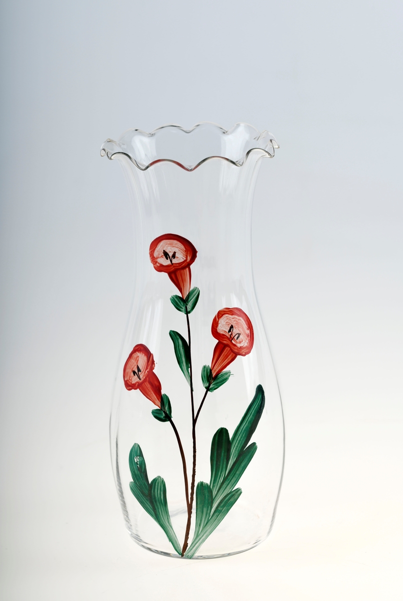 En glassvase av klart glass med påmalt dekor. Den smalner noe i halsen før den "bretter" seg ut. Kanten oppe er bølgete (tungekant). På den ene siden av vasen er det påmalt blomsterdekor. Det er tre røde, klokkeformede blomster med svarte stilker og detaljer. Bladene er grønne og avlange.